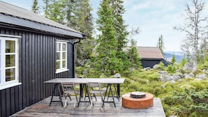 A wooden deck with a table and chairs, a small fire pit, and a building with a dark exterior and white windows. - Nice home in Sjusjøen with WiFi (Sjusjøen)
