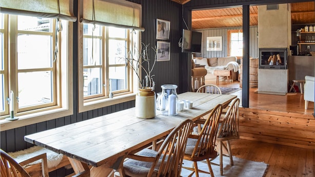 A wooden dining table with chairs, a vase with branches, and a fireplace in a room with wooden walls and large windows. - Nice home in Sjusjøen with WiFi (Sjusjøen)