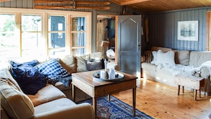 A cozy living room with a wooden ceiling, a sofa set, a coffee table with candles, and a large window with multiple panes. - Nice home in Sjusjøen with WiFi (Sjusjøen)
