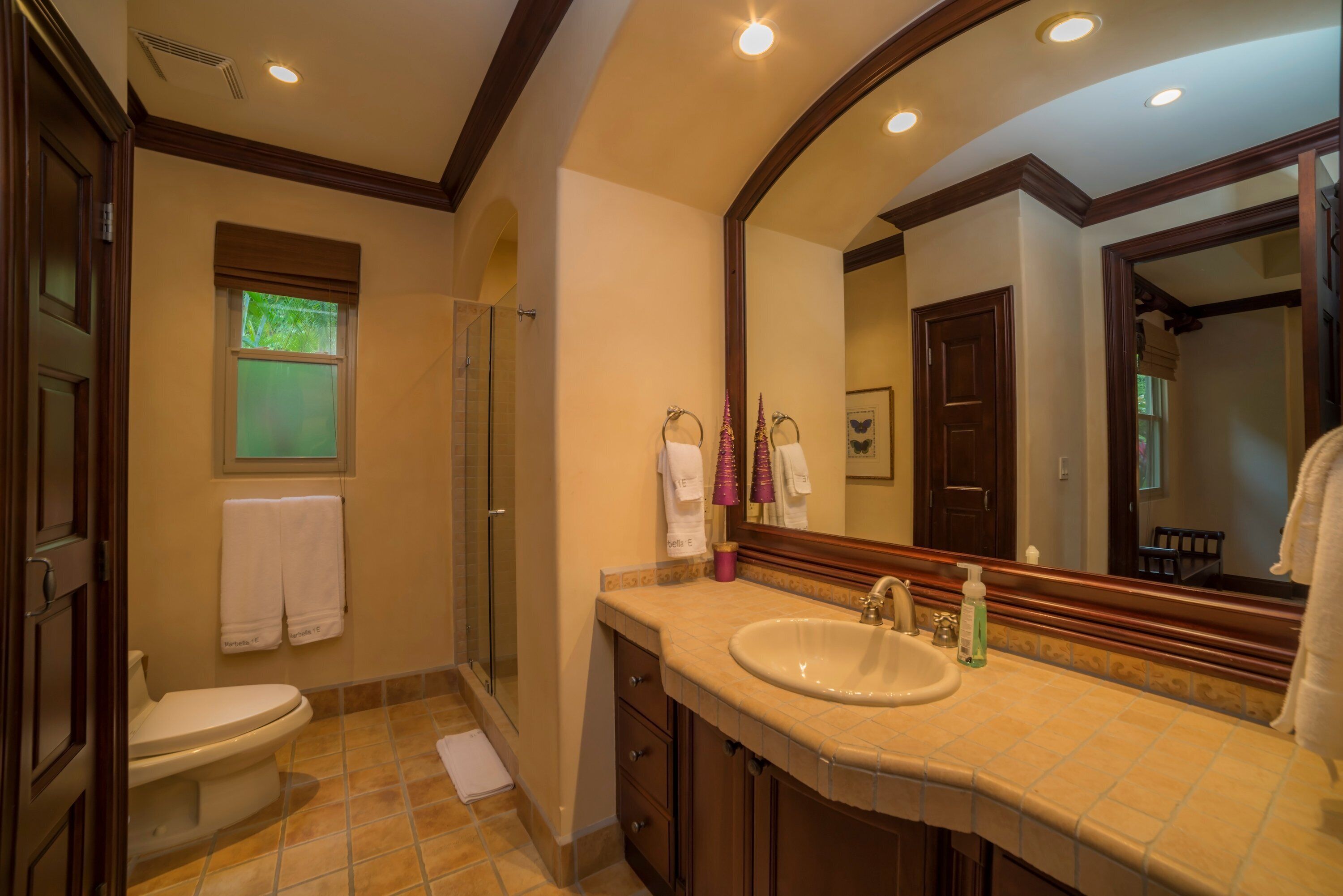 A bathroom with a toilet, sink, and shower. There are towels hanging on the wall and a mirror above the sink.