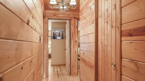 A wooden hallway with a chandelier, wooden walls, and a door leading to another room. - Log Cabin in the Woods (Arkdale)