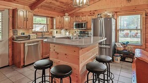 A wooden cabin-style kitchen with a central island, stainless steel appliances, and bar stools. - Log Cabin in the Woods (Arkdale)
