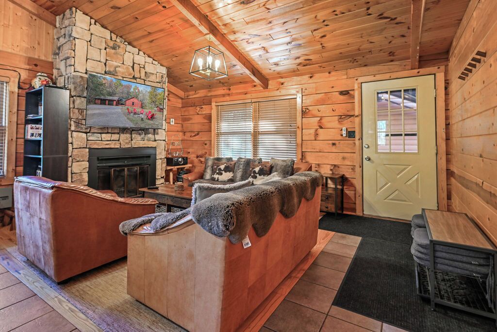 Ein gemütliches Blockhaus-Interieur mit Kamin aus Stein, einer Couch mit Felldecke und Holzbalkendecke.