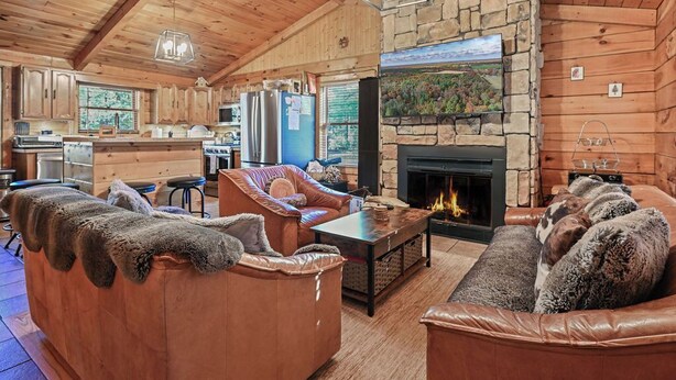A cozy cabin interior with a stone fireplace, leather sofas, and a wooden ceiling. - Log Cabin in the Woods (Arkdale)