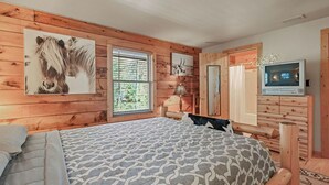 A bedroom with a bed, wooden walls, a dresser, a television, and artwork. - Log Cabin in the Woods (Arkdale)