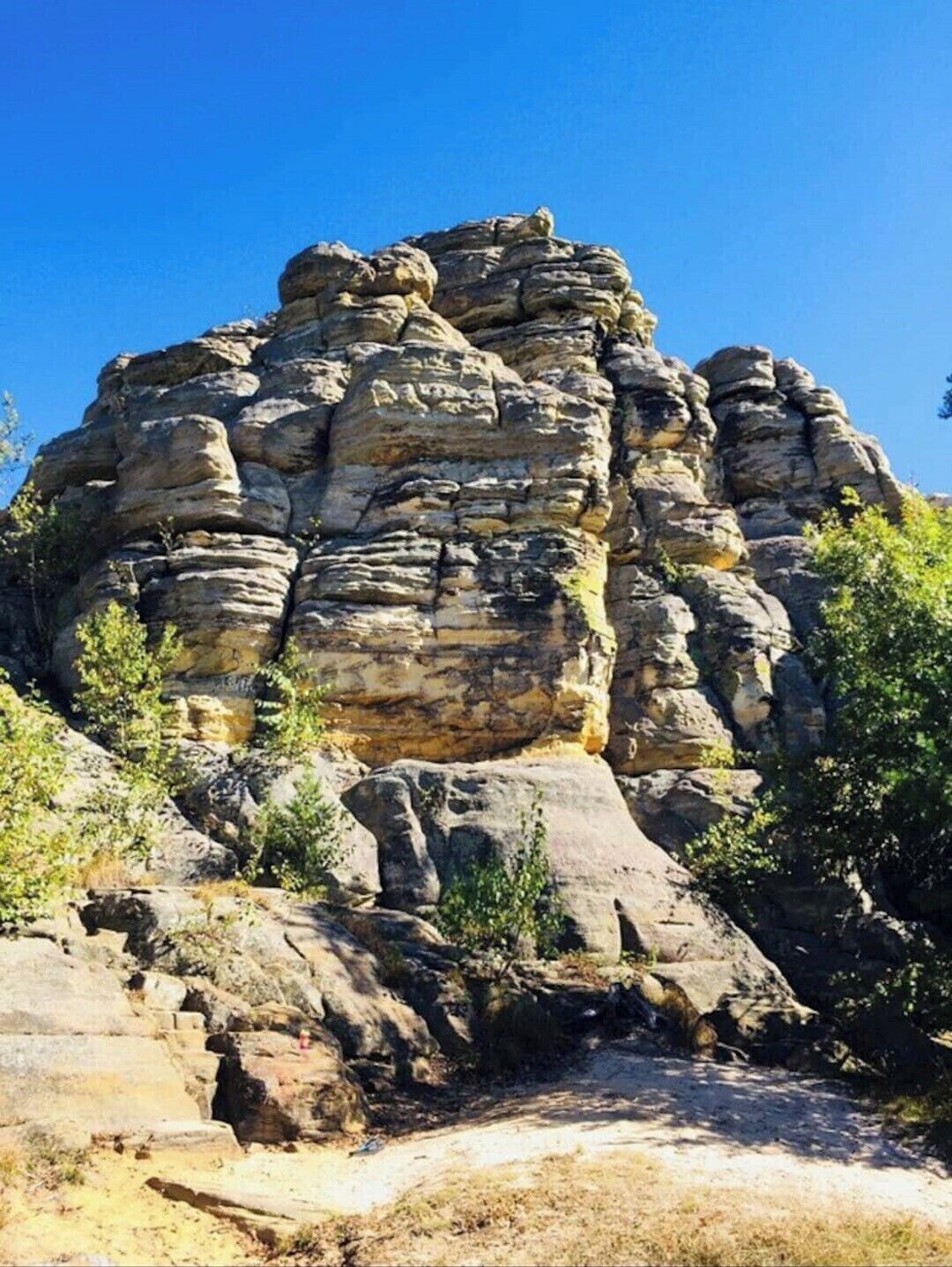 A rocky cliff with layered rock formations and sparse vegetation.
