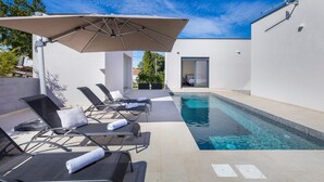 A modern outdoor pool area with lounge chairs and a large umbrella. - Gorgeous home in Vintijan with sauna (Vintijan)