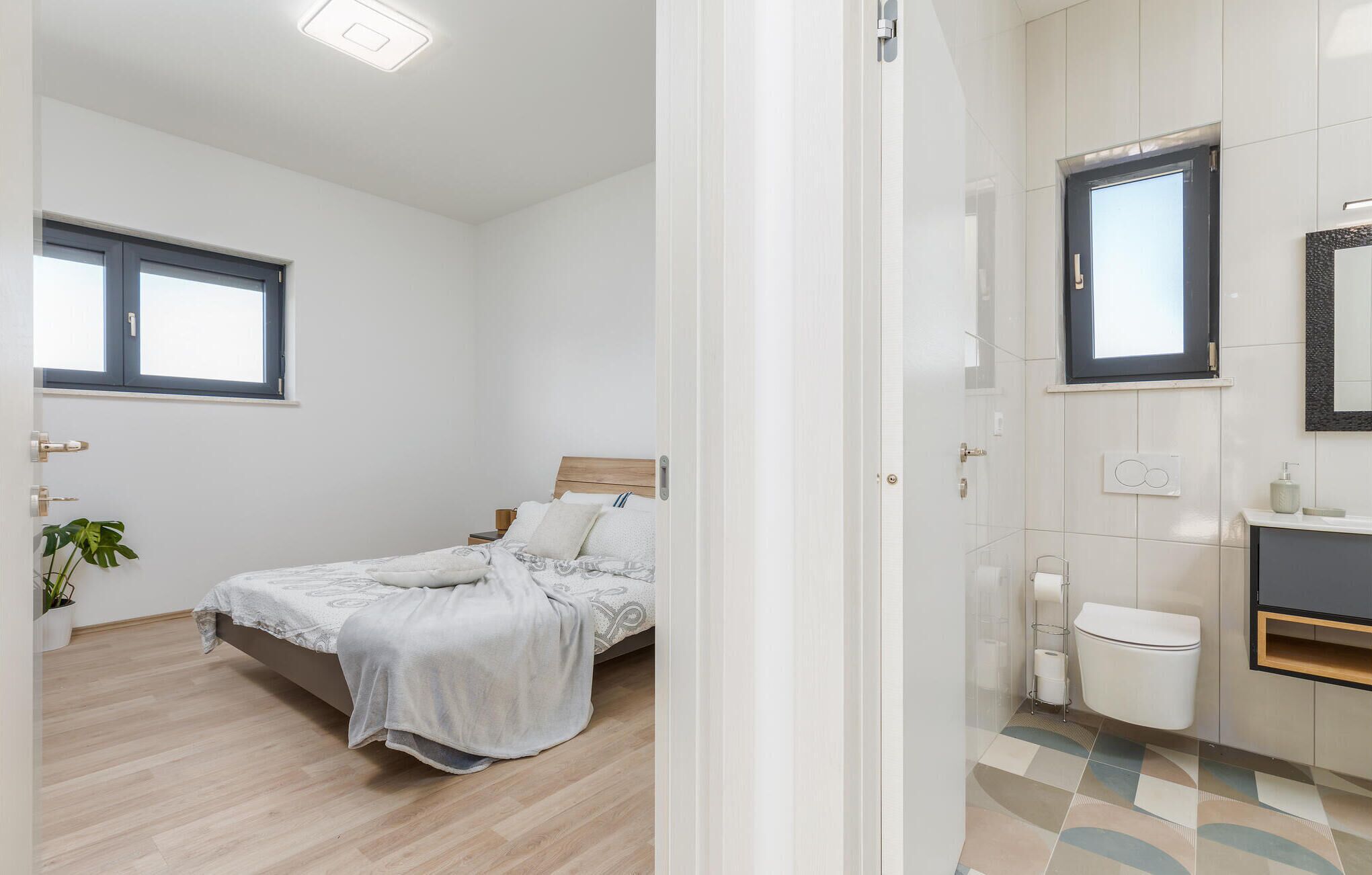 A bedroom with a bed, a bedside table, a window, and a potted plant.