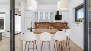 A modern kitchen with white cabinetry, a wooden countertop, and three white bar stools. - Gorgeous home in Vintijan with sauna (Vintijan)