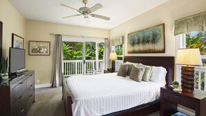 Une chambre à coucher comprenant un lit, un ventilateur de plafond, une télévision, une commode et une fenêtre avec des rideaux.