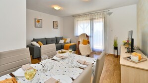 A modern living room with a grey sofa, a dining table set for four, and a large window with sheer curtains. - Stunning home in Seketin (Seketin)