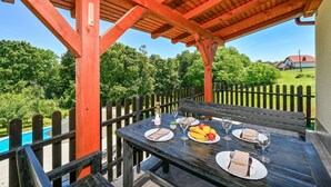 An outdoor wooden table set for dining with a view of a swimming pool and greenery. - Stunning home in Seketin (Seketin)