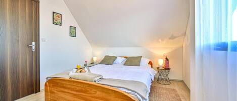 Een slaapkamer met een houten bed, een nachtkastje met een lamp en een raam met gordijnen.