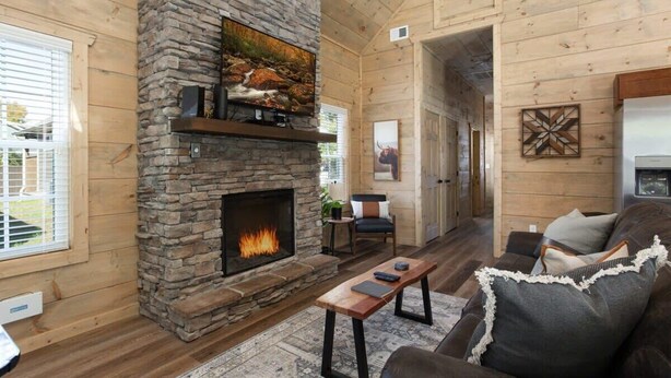A cozy cabin interior with a stone fireplace, wooden walls, a sofa, and a dining table.