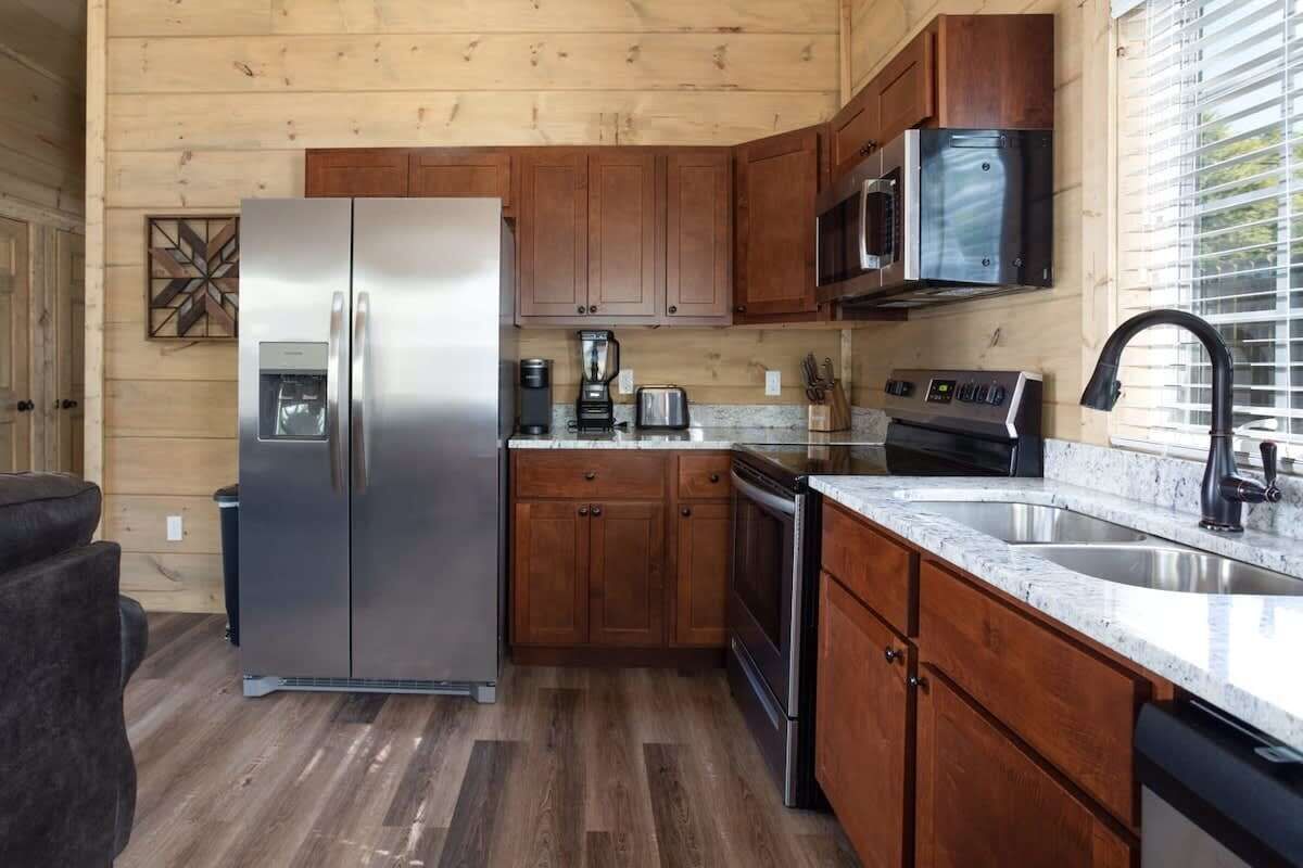 A compact kitchen with wooden cabinets, a stainless steel refrigerator, a microwave, a stove, and a sink.