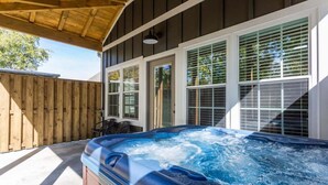 A hot tub under a covered patio with a wooden fence and windows.