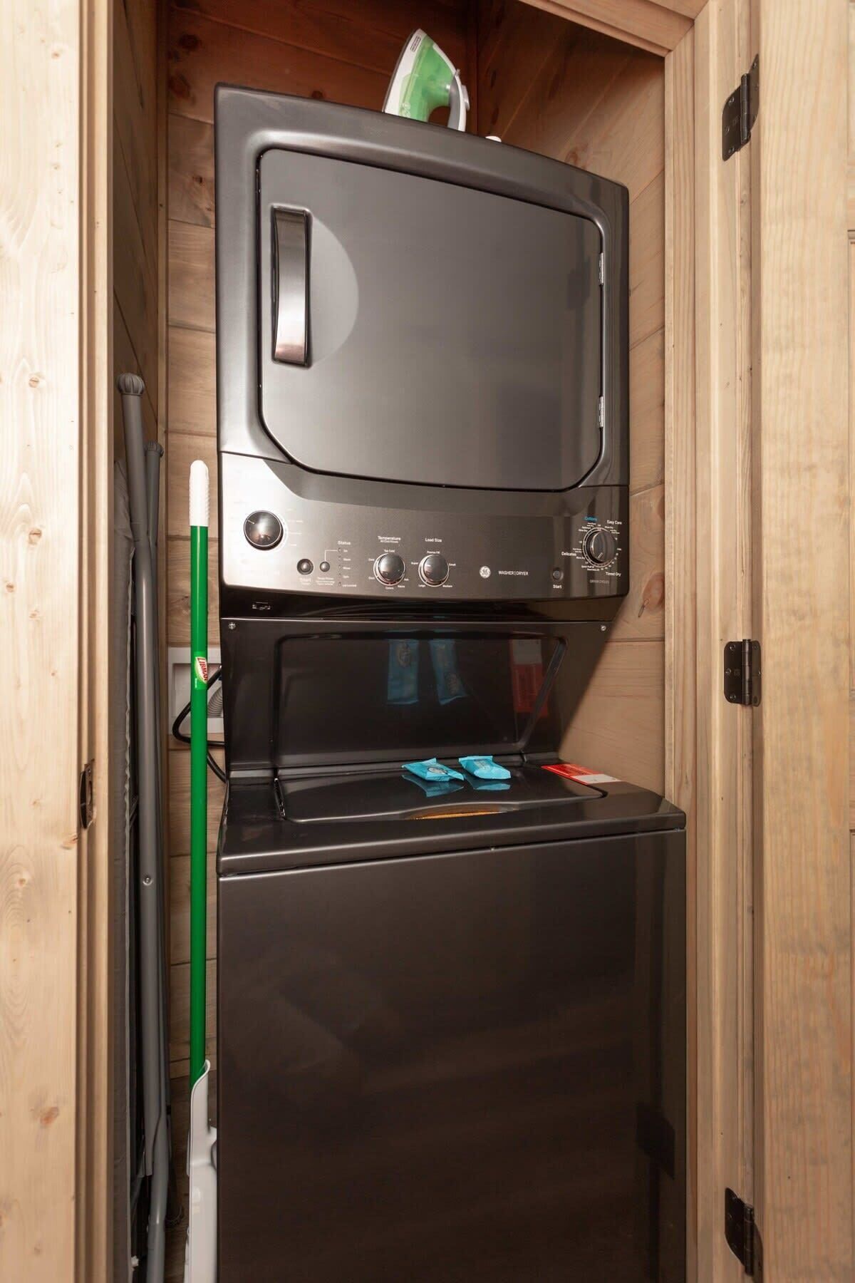 A compact kitchen with a microwave and oven, wooden cabinets, and a green cleaning tool.