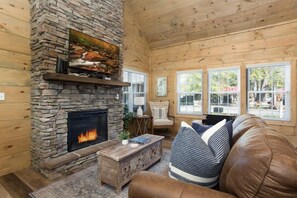 A cozy living room with a stone fireplace, wooden walls, and a leather couch.