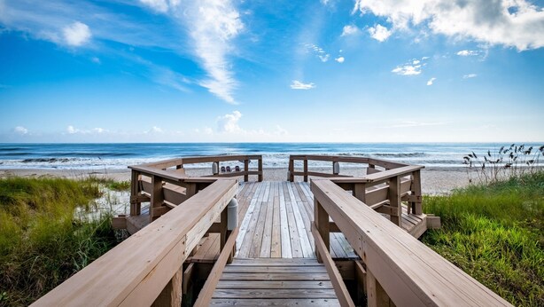 A wooden boardwalk leading to a beach with a clear sky and ocean view.