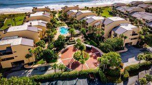 A resort with multiple buildings, a central pool, and a beach view.
