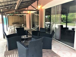 An outdoor patio area with wicker furniture, a table, and a glass door leading to a covered outdoor space.