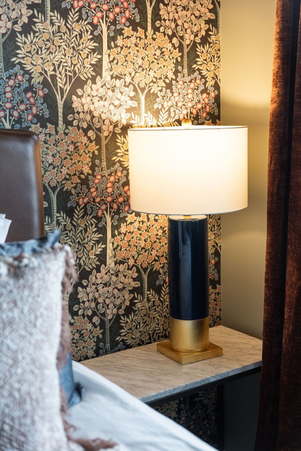 A lamp on a bedside table with a floral wallpaper background.