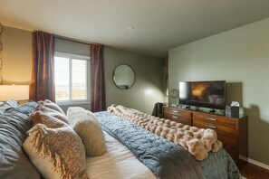 Ein Schlafzimmer mit Bett, Fernseher, Kommode und einem Fenster mit Vorhängen.