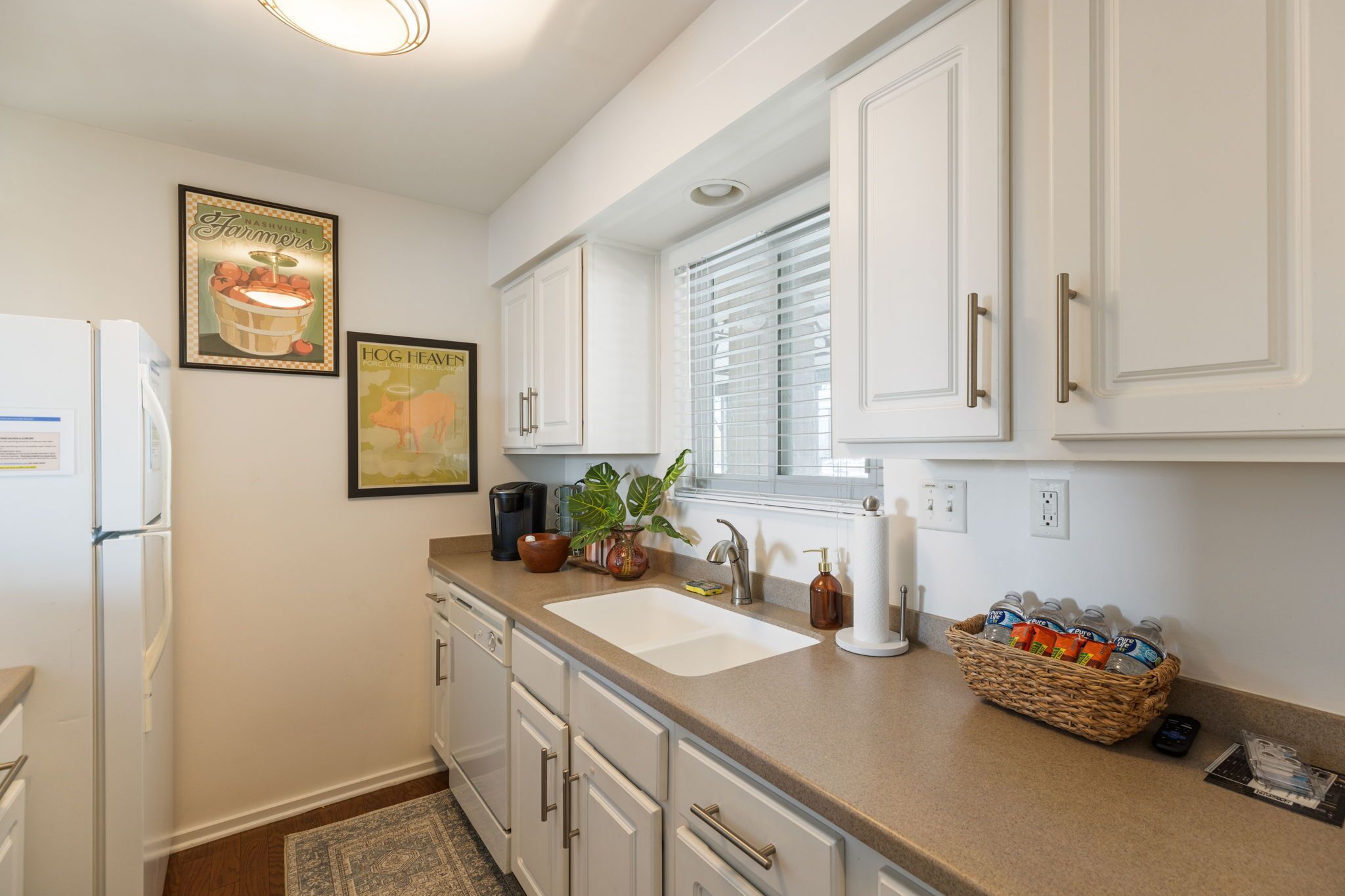 A kitchen with white cabinets, a sink, a refrigerator, and a window with blinds.
