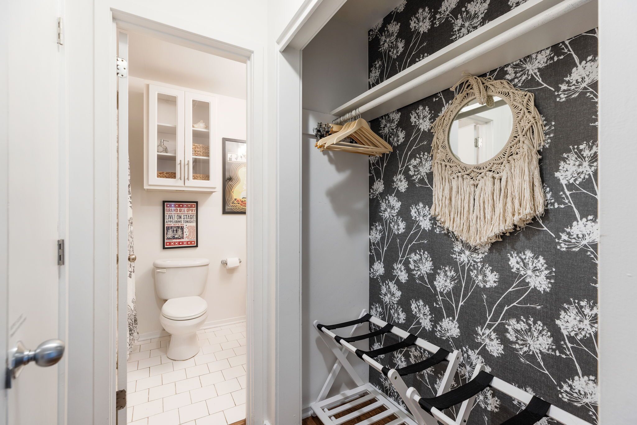 Une salle de bain avec des toilettes blanches, un meuble blanc et un miroir orné d’une décoration en macramé accrochée au mur.
