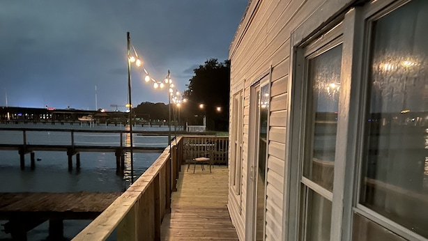 A wooden deck leading to a building with large windows, overlooking a body of water.