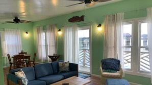 A living room with a sofa, coffee table, and a chair. There is a dining table with chairs and a window with curtains.