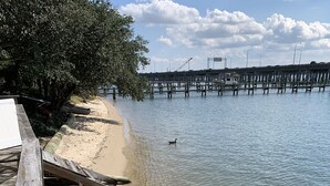 A wooden pier extending into calm water with a clear sky and a distant bridge.