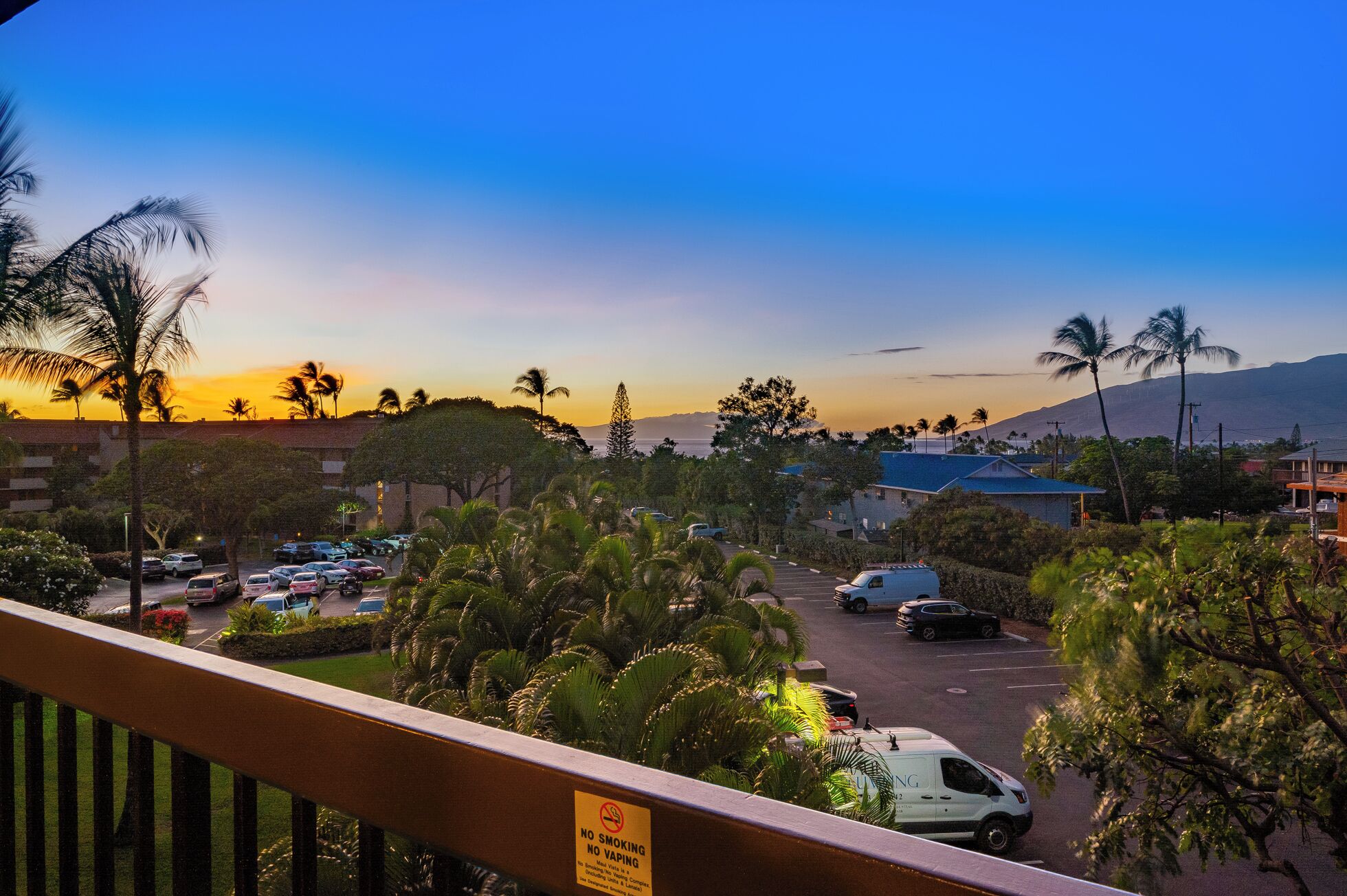 A parking lot with several cars, surrounded by palm trees and buildings.