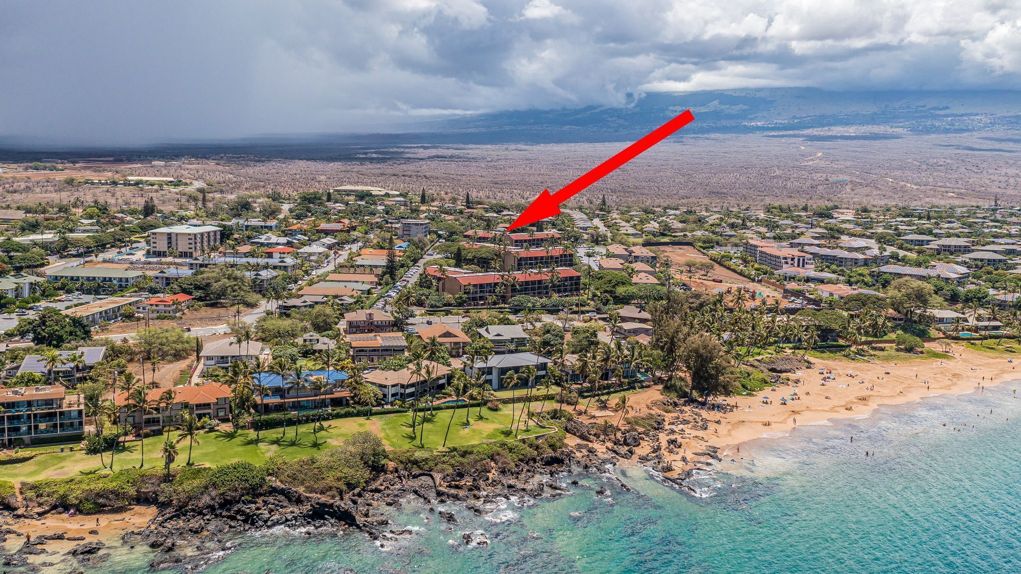 Vista aérea de una zona turística costera con varios edificios, una playa y un litoral rocoso.