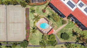 An aerial view of a property with a swimming pool, tennis courts, and a building with solar panels.