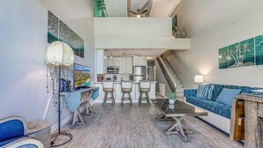 A spacious living area with a kitchen, bar area, and a staircase leading to an upper level. - Great location, Stylish Beachy Condo With Upgraded Amenities & Ocean View (Kihei)