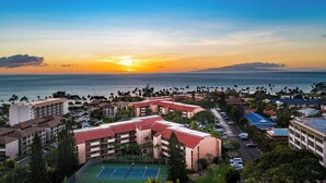 A resort with multiple buildings, a tennis court, and a view of the ocean at sunset. - Great location, Stylish Beachy Condo With Upgraded Amenities & Ocean View (Kihei)