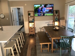 A modern kitchen with a wooden dining table, bar stools, and a TV displaying a commercial. - Sea Colony-Perfect Beach Getaway-Newly Renovated (Bethany Beach)