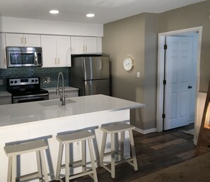A modern kitchen with white cabinets, stainless steel appliances, and a central island with stools. - Sea Colony-Perfect Beach Getaway-Newly Renovated (Bethany Beach)