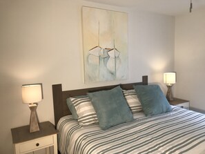 A neatly made bed with striped bedding, two bedside lamps, and a wall-mounted abstract painting. - Sea Colony-Perfect Beach Getaway-Newly Renovated (Bethany Beach)