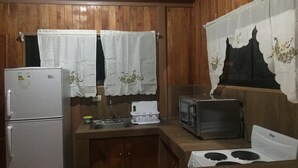 A compact kitchen with wooden walls, a refrigerator, a microwave, and a stove. - Don Beto House (Provincia de Puntarenas)