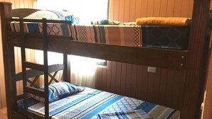 A bunk bed with a patterned bedspread and pillows, wooden walls, and a window with curtains. - Don Beto House (Provincia de Puntarenas)