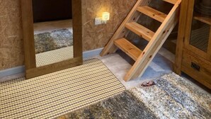 Una habitación con escalera de madera, un espejo y vistas a otra habitación con una cama y estanterías.
