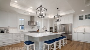A modern kitchen with white cabinetry, a large island with bar stools, stainless steel appliances, and pendant lighting.