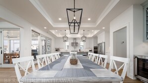 A spacious dining area with a large wooden table, white chairs, and pendant lighting.
