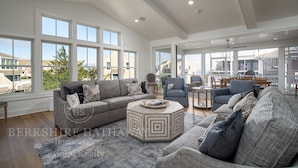 A spacious living room with a high ceiling, large windows, and a modern design.