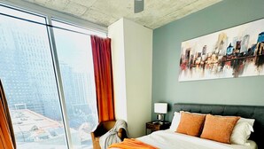 A hotel room with a large bed, a ceiling fan, a city view through the window, and a painting on the wall. - The Urban Oasis in Midtown (Atlanta)