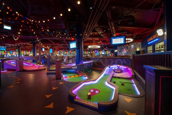 A vibrant arcade with neon-lit pinball machines and a bar area.