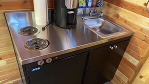 Et kompakt køkken med komfur i rustfrit stål, vask og sort køleskab.