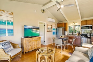 A spacious living area with a large TV, wicker furniture, and a kitchen with modern appliances.